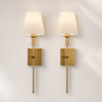 Pair of brass wall sconces with cream fabric shades and rectangular backplates on a pale wall.