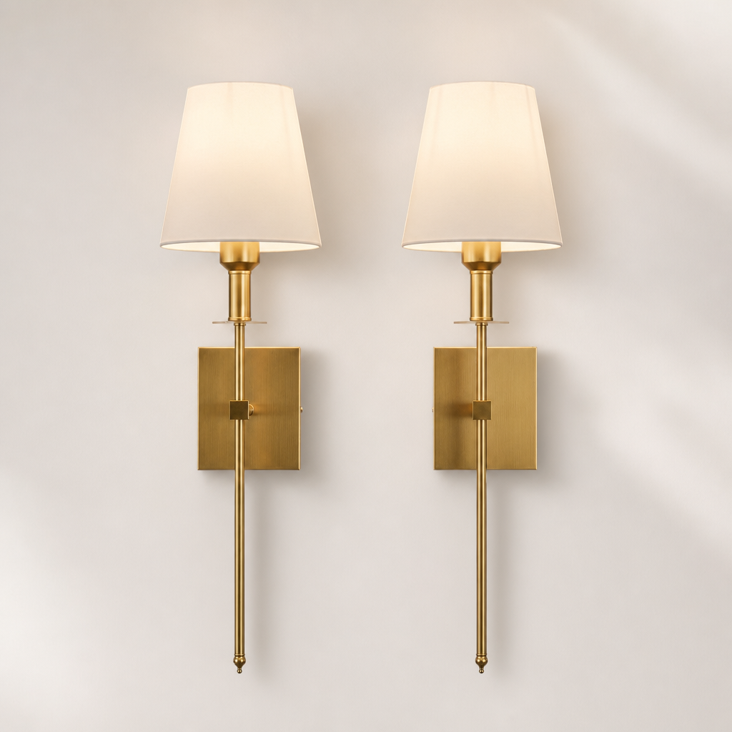 Pair of brass wall sconces with cream fabric shades and rectangular backplates on a pale wall.