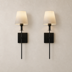 Pair of black wall sconces with cream fabric shades on a pale neutral wall.