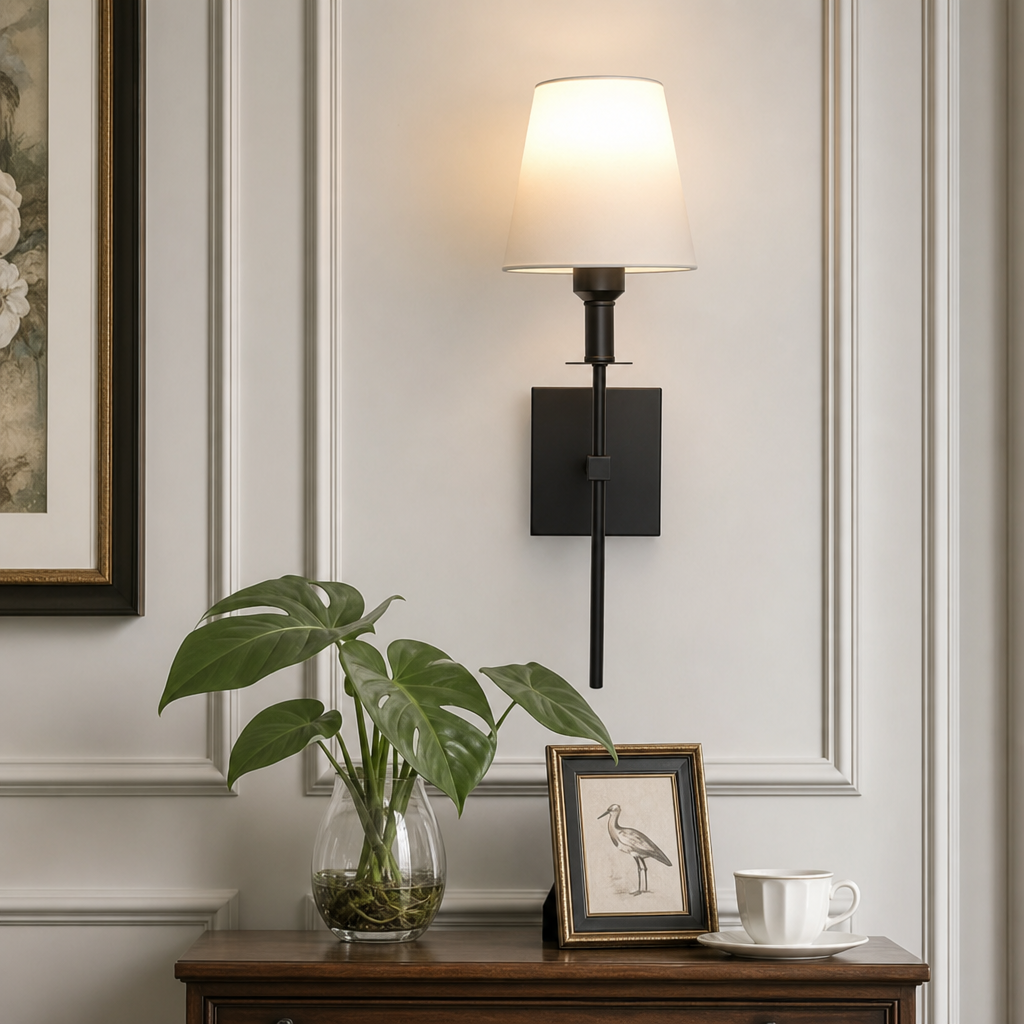 Black wall sconce with glowing white shade above a wooden table with a small leafy plant.