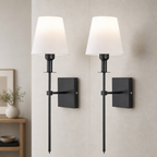 Two black wall sconces with white fabric shades mounted on a light gray wall.