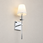 Chrome wall sconce with a glowing white fabric shade on a light neutral wall.