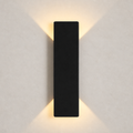 Black rectangular wall sconce casting warm light upward and downward on a plain wall.