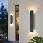 Two slim black outdoor wall sconces cast warm up and down light on a modern exterior wall.