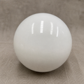 Glossy white spherical lamp shade on a neutral fabric surface.