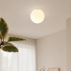 Glowing round ceiling light mounted above sheer curtains and a leafy indoor plant.