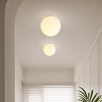 Two glowing spherical ceiling lights illuminate a minimalist hallway with white walls and a plant.