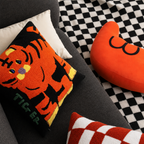 Tiger cushion and orange heart pillow on a dark sofa with a checkered rug.