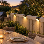 Lights along a backyard fence beside an outdoor dining and barbecue area.