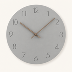 Round gray wall clock with thin black numbers and wooden hands on a light neutral background.