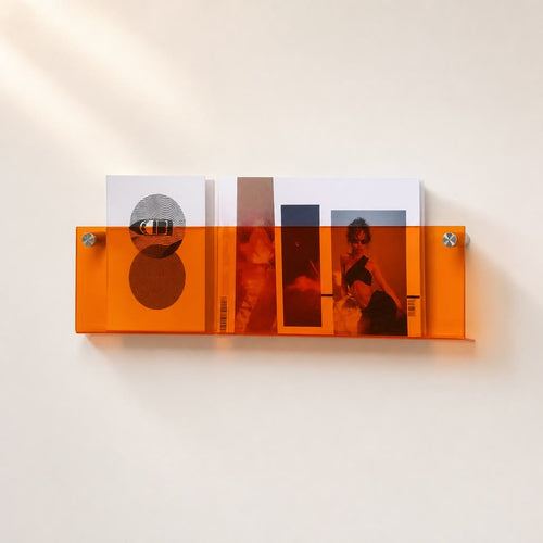 Orange translucent wall shelf holding magazines on a light wall.