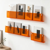Translucent orange acrylic wall shelves display books and magazines on a white wall.