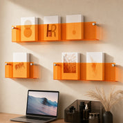 Transparent orange acrylic wall shelves display books above a desk with a laptop and small decor.