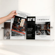 Clear acrylic magazine wall rack holding home design magazines with a hand placing one inside.