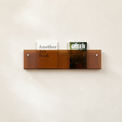 Amber transparent wall shelf holding two upright books on a light neutral wall.