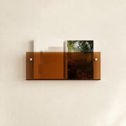 Amber wall shelf holding two books with white mounting screws on a plain light wall.