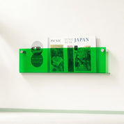 Transparent green wall-mounted magazine holder with publications inside on a white wall.