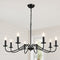 Black six-light candle chandelier with glowing bulbs hanging from a chain in a bright room.