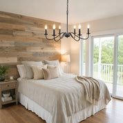 Black six-light candle chandelier hanging above a cozy bed.