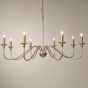 Brass chandelier with eight candle-style lights and curved arms on a pale gray background.