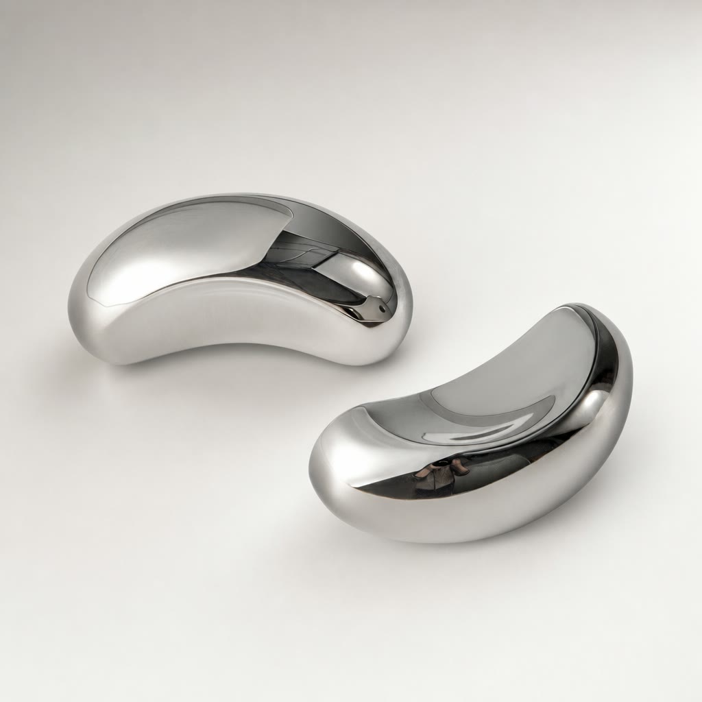 Two polished silver curved earbud-like devices on a clean light surface.