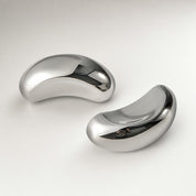 Two polished silver curved earbud-like devices on a clean light surface.