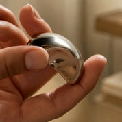 Hand holding a small polished silver bean-shaped metal object.