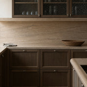 Dark wood kitchen cabinets with beige stone countertop and textured glass upper doors.