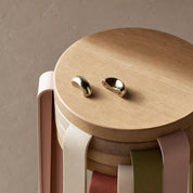 Two polished gold earbud-like pieces rest on a round wooden stool with pastel ribbon accents.
