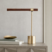 Brass and walnut desk lamp with a cylindrical base on a sideboard beside stacked books.