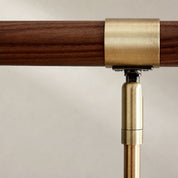 Brushed brass railing bracket clamping a dark wooden handrail against a pale wall.