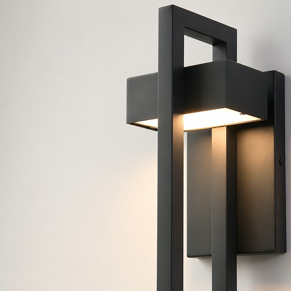 Black rectangular wall sconce with warm light glowing against a pale wall.