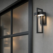 Black rectangular outdoor wall light glowing warmly beside a modern glass door.