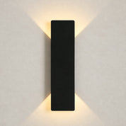 Black rectangular wall sconce casting warm light upward and downward on a plain wall.