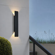 Black rectangular outdoor wall light casts warm beams on a white wall beside stairs.