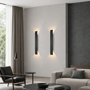Two slim black vertical wall sconces cast warm light on a modern living room wall.