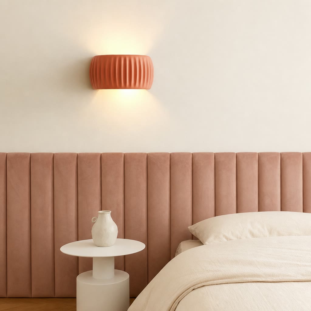 Terracotta ribbed wall sconce glowing above a pink upholstered bed headboard.