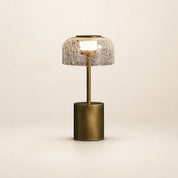 Brass table lamp with crackled glass dome shade glowing on a pale neutral background.