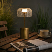 Brass table lamp with a glowing crackled glass dome shade on a wooden table.