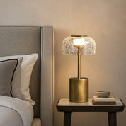 Gold bedside lamp with cracked glass dome shade glowing on a nightstand.