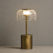 Gold table lamp with cracked glass shade glowing on a neutral tabletop
