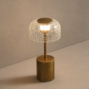 Gold table lamp with a cracked clear glass shade glowing warmly on a gray surface.