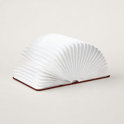 White accordion-style open book lamp with fan-shaped pages on a dark red base.