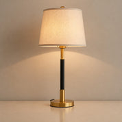 Gold and black table lamp with a cream fabric shade glowing on a neutral tabletop.
