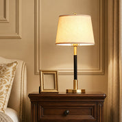 Gold and black table lamp with a glowing fabric shade on a wooden bedside table.