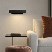 Black rectangular wall light above a side table beside a beige armchair with a brown cushion.