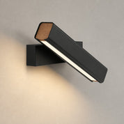 Black angled wall light with wood end caps mounted on a textured wall.