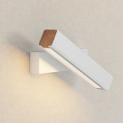 White wall-mounted linear lamp with wood accents casting warm light on a textured wall.