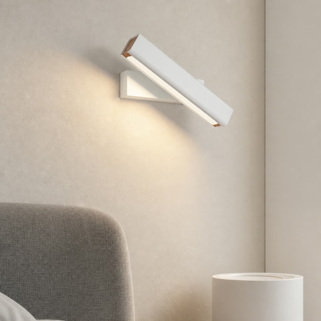 White angled wall lamp glowing warmly above a bedside corner.