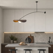 Curved pendant lamp over a modern kitchen with white cabinets, stone backsplash, and island stools.